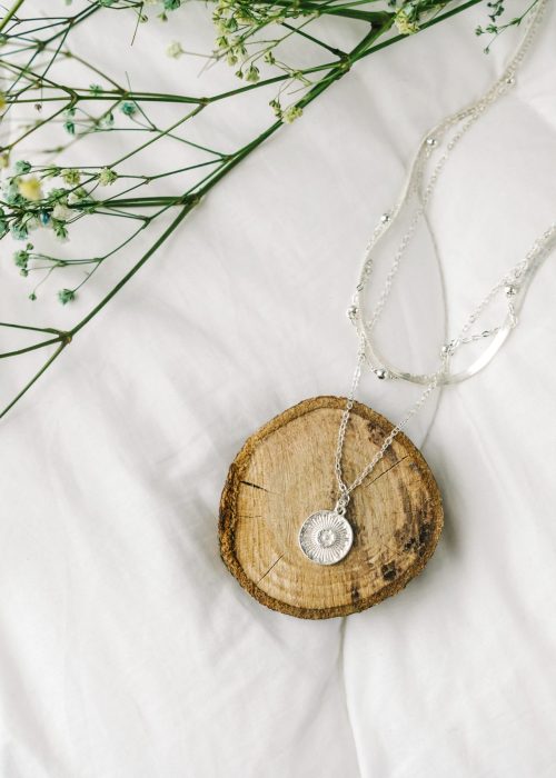 Imitation jewelry, silver bijouterie chain on white textile background. Dry little flowers.